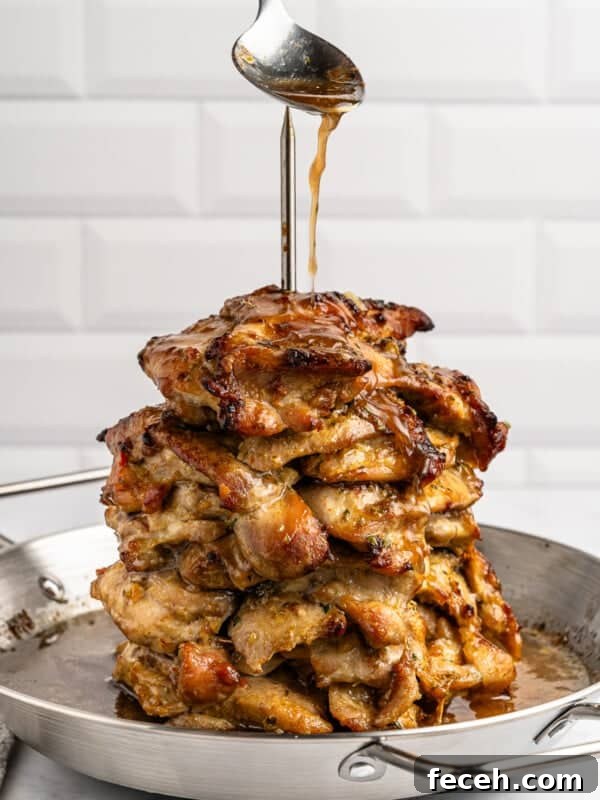 A stack of grilled chicken pieces skewered on a spit in a pan. A spoon drizzles sauce over the top, enhancing the golden-brown, juicy appearance of the chicken. The background features a white, tiled wall design.