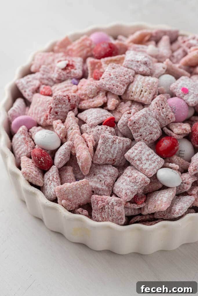 Valentine’s Day muddy buddies made with pink candy melts, powdered sugar, and Valentine’s M&M’s in a white dish