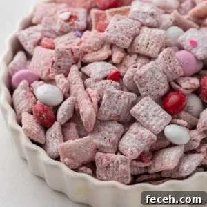Valentine’s Day muddy buddies made with pink candy melts, powdered sugar, and Valentine’s M&M’s in a white dish