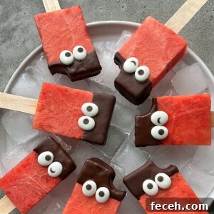 Rectangular watermelon popsicles on sticks, partially dipped in chocolate and decorated with candy eyes, are arranged on a plate of ice. One popsicle has a small bite taken out—making these fun bites perfect for healthy food recipes.