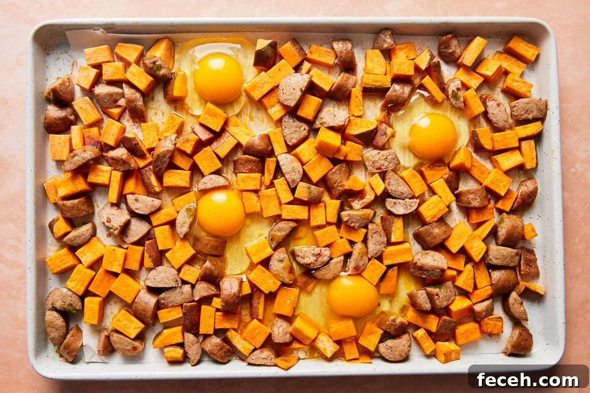Sheet pan with eggs nestled among roasted sweet potatoes and sausage
