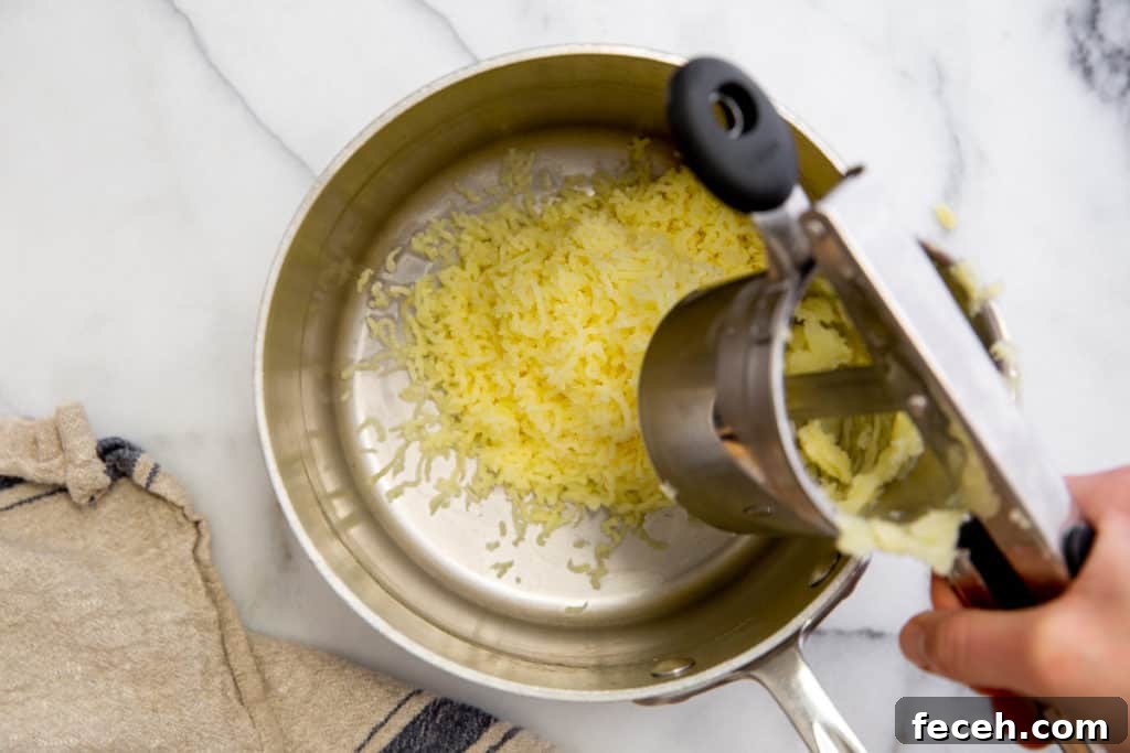 A hand squeezing cooked potatoes through a potato ricer.