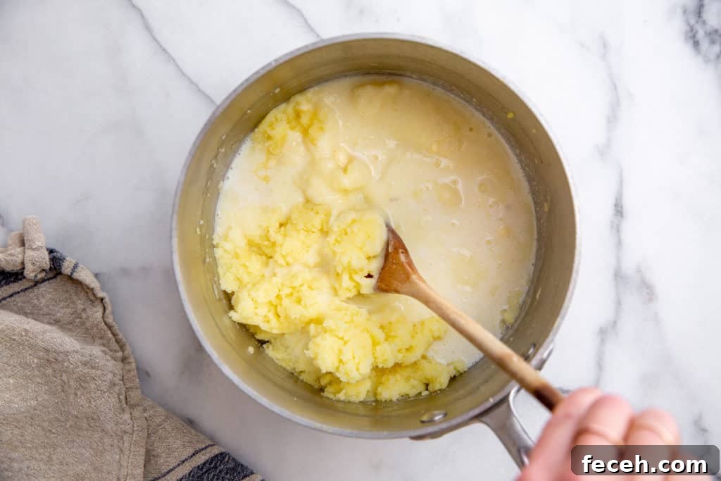 A hand stirring milk into the potatoes in the pot. 
