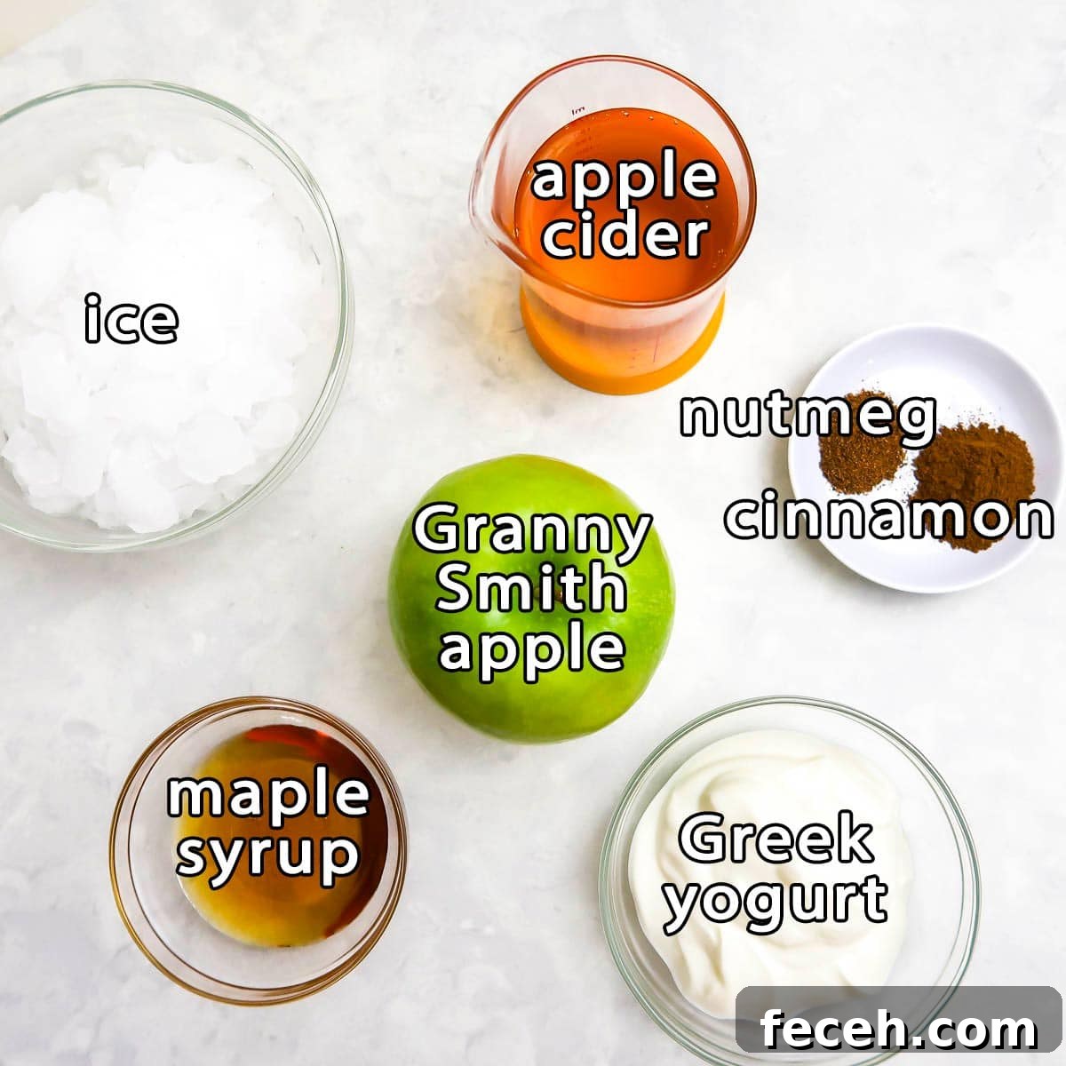 Overhead view of ingredients - ice, apple cider, granny smith apple, maple syrup, greek yogurt, nutmeg, and cinnamon.