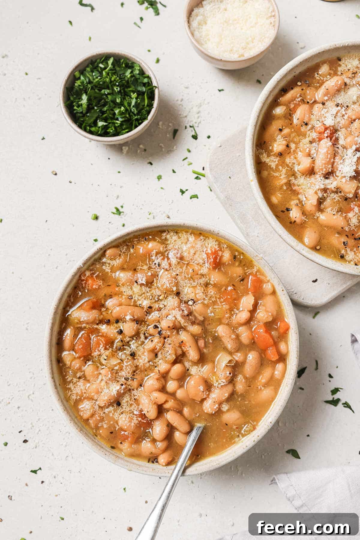Instant Pot Navy Bean Soup Recipe for Creamy, Hearty Comfort 13 A bowl of bean soup garnished with cheese and herbs, with a spoon in it, accompanied by small bowls of cheese and chopped herbs on the side.