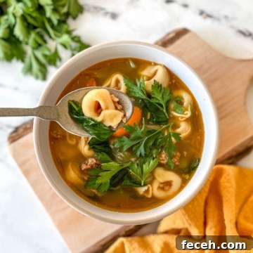 A bowl of tortellini soup sits on a rustic wooden cutting board with a yellow linen and a bunch of parsley.