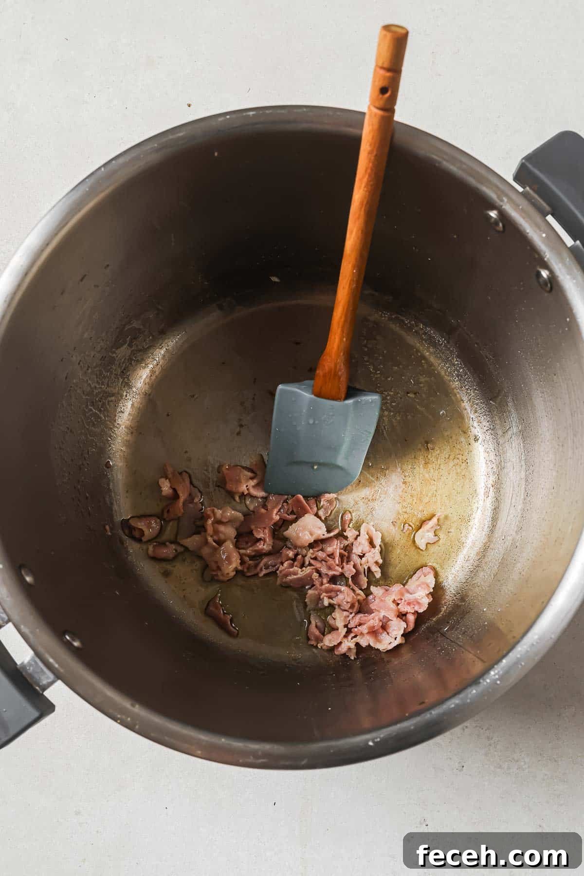 Instant Pot Navy Bean Soup Recipe for Creamy, Hearty Comfort 7 A pot with cooked bacon pieces and a silicone spatula.