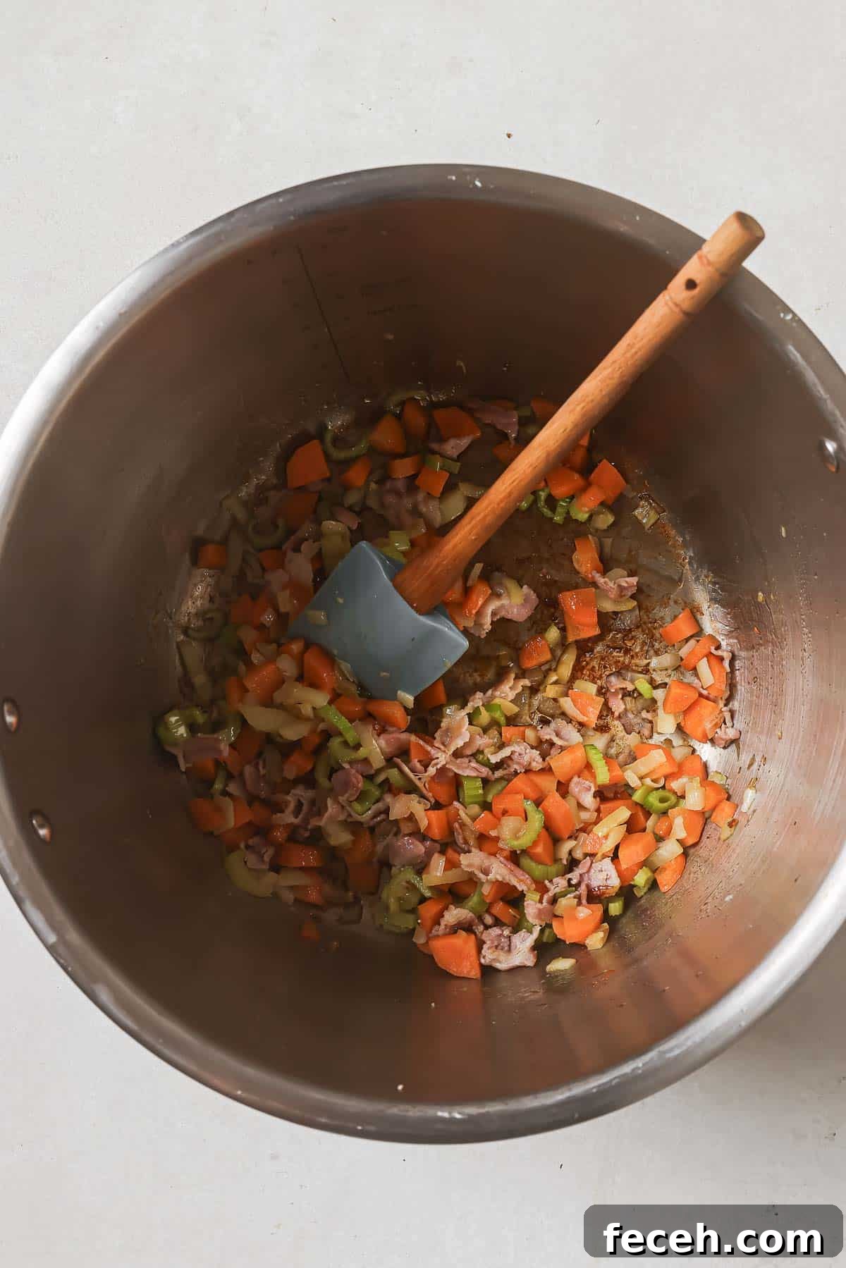 Instant Pot Navy Bean Soup Recipe for Creamy, Hearty Comfort 9 Diced vegetables with a wooden spatula in a stainless steel cooking pot.