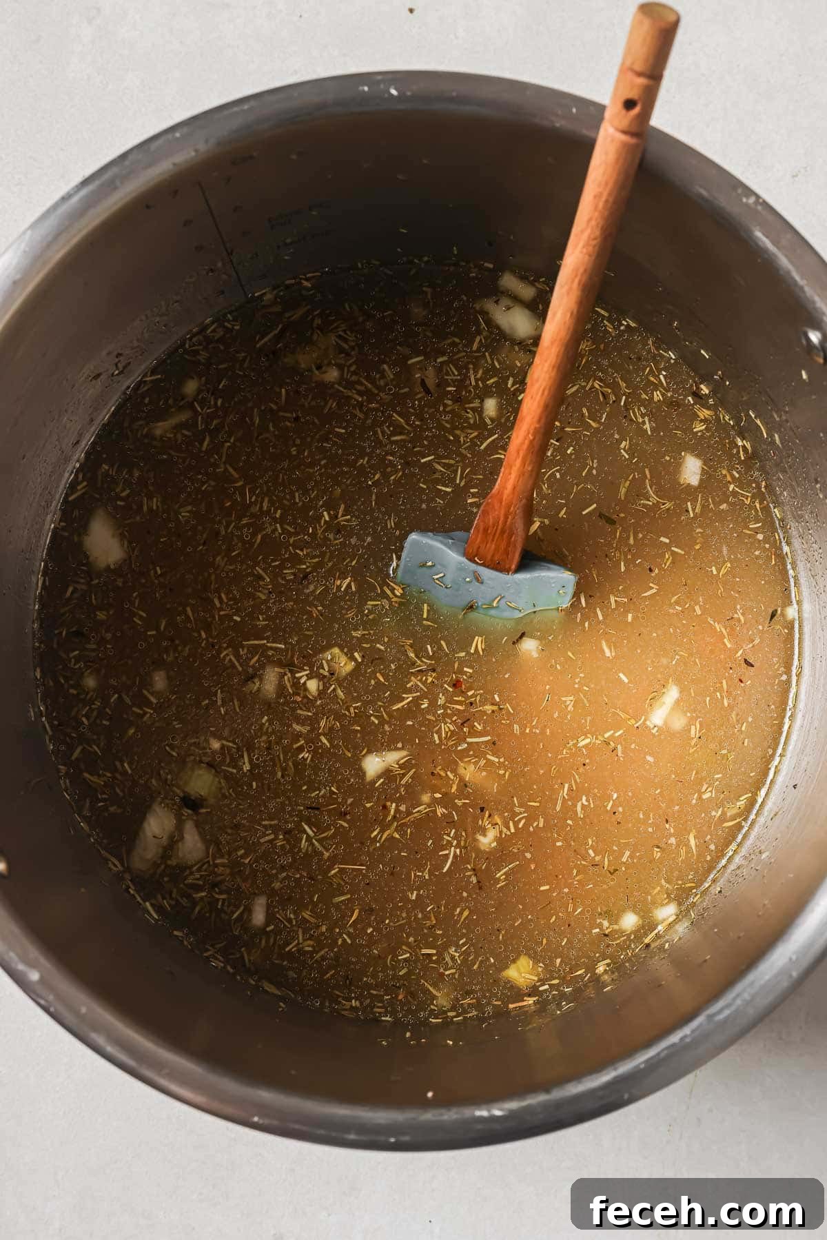 Instant Pot Navy Bean Soup Recipe for Creamy, Hearty Comfort 10 A pot of broth with herbs and vegetables, with a wooden spoon inside.