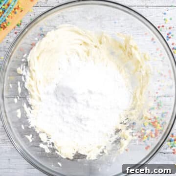 Powdered sugar added to creamed butter in glass bowl.