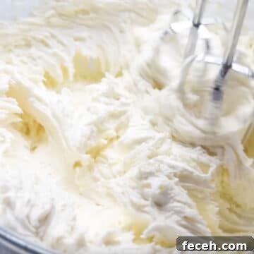Frosting ingredients being whipped with hand-held mixer.