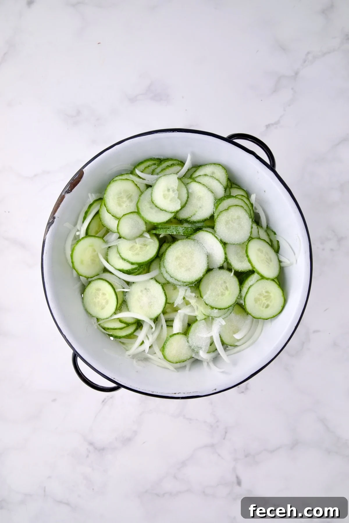 Cucumbers and onions in white distressed colander sprinkled with salt.