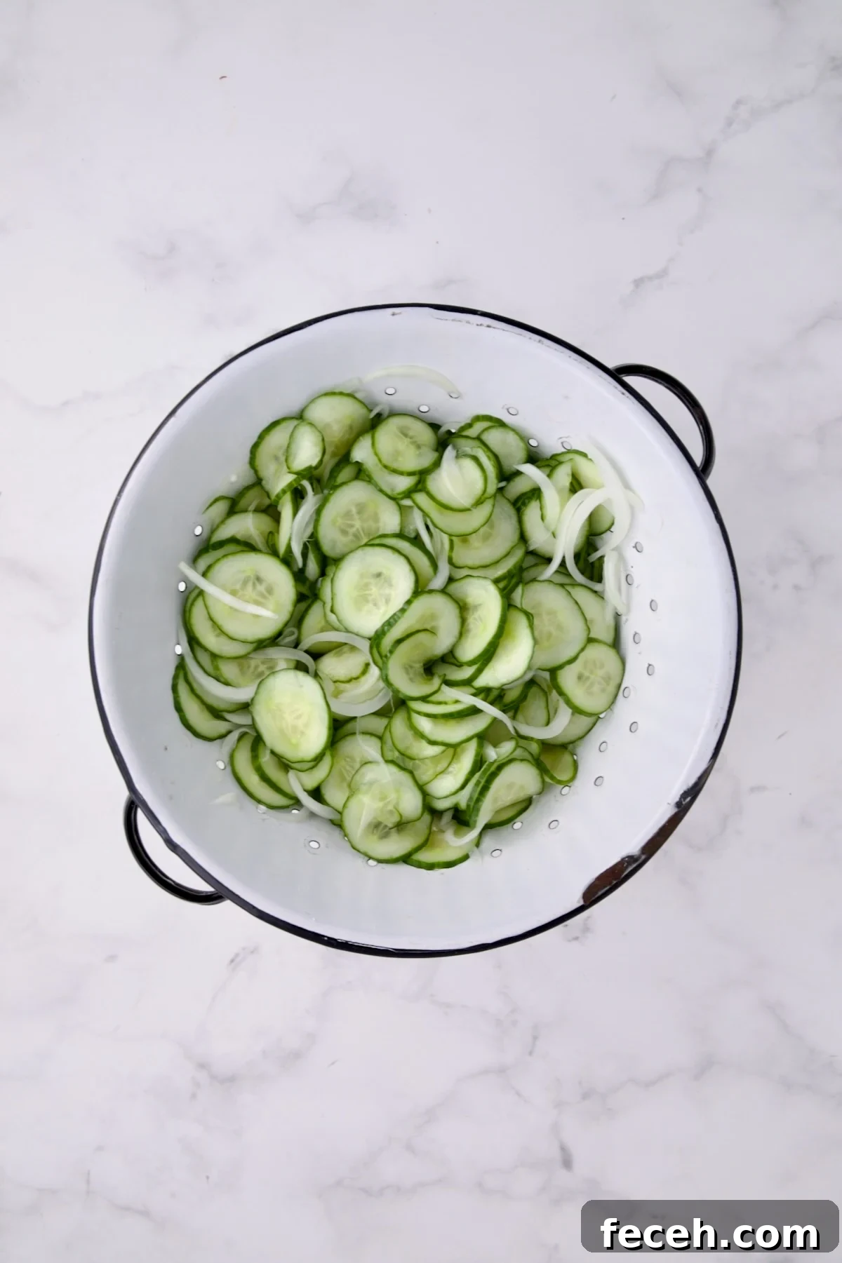 Cucumbers and onions in white distressed colander after being salted and drained.