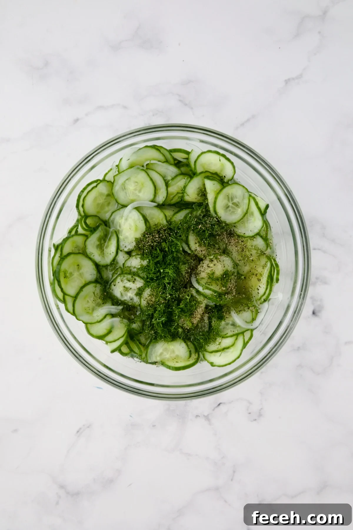 Cucumbers, onions, dressing and dill in glass bowl.