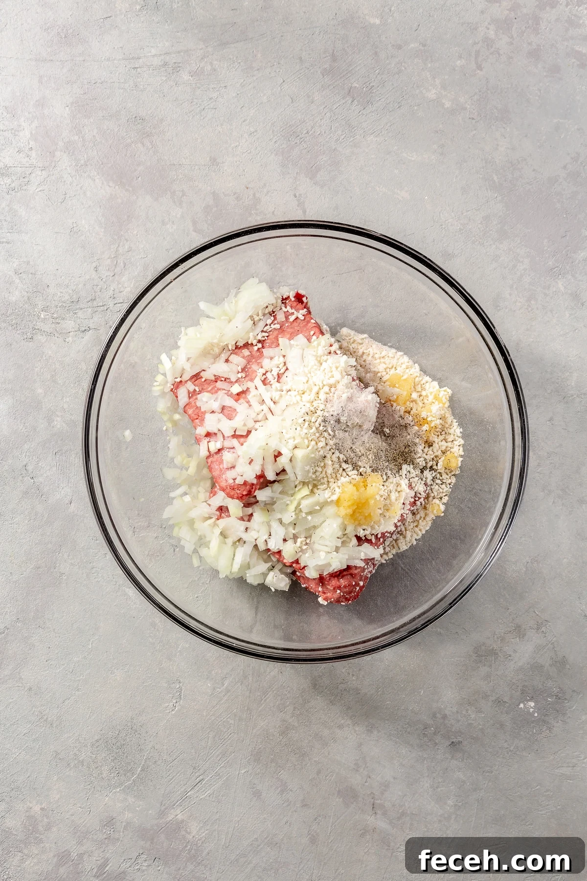 A variety of ingredients have been added to the top of the ground beef. It all sits in a glass bowl.