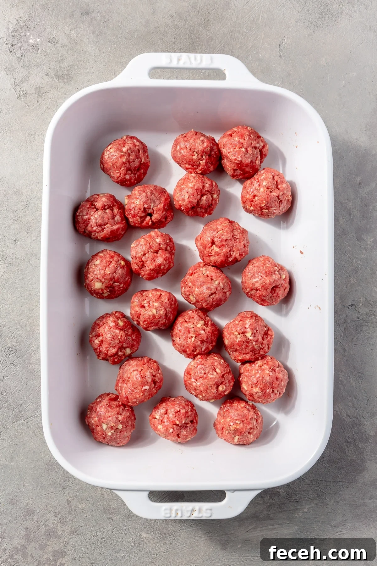 The ground beef mixture has been rolled into meatballs of which sit in a white baking dish.