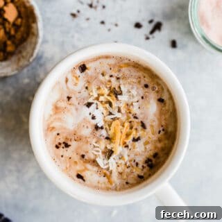 Toasted coconut hot chocolate in a mug topped with coconut cream, toasted coconut, and chocolate shavings.