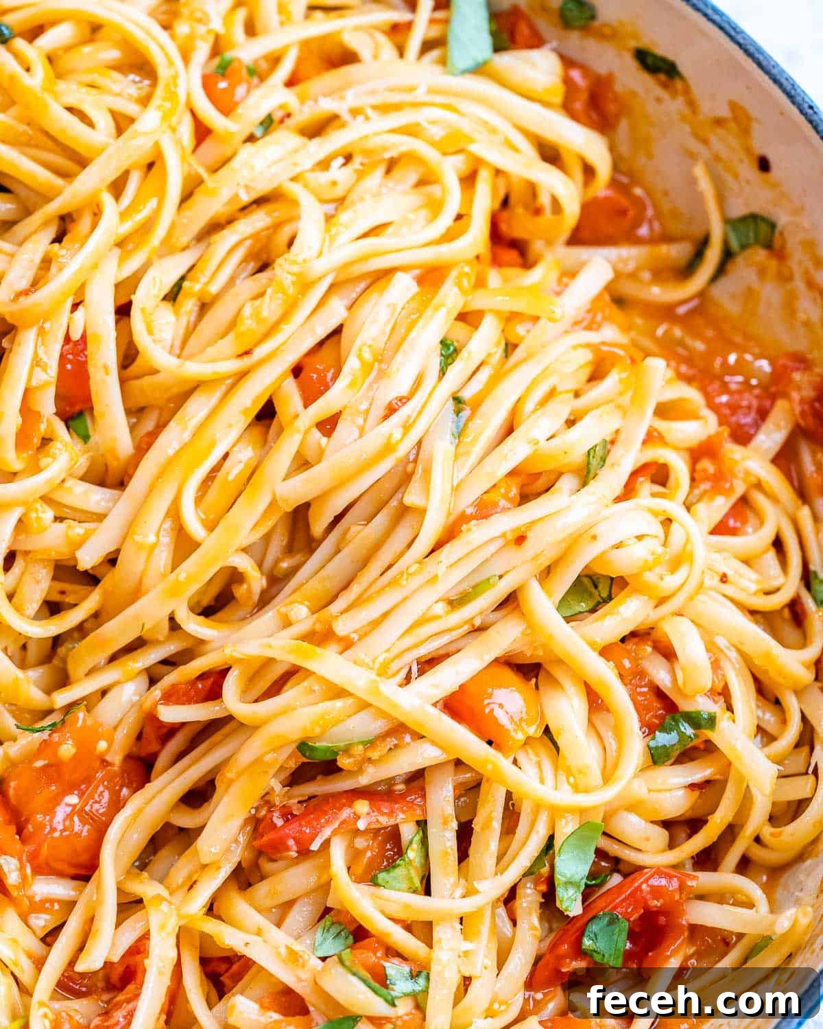Pasta being tossed into the skillet with tomato basil sauce using kitchen tongs.