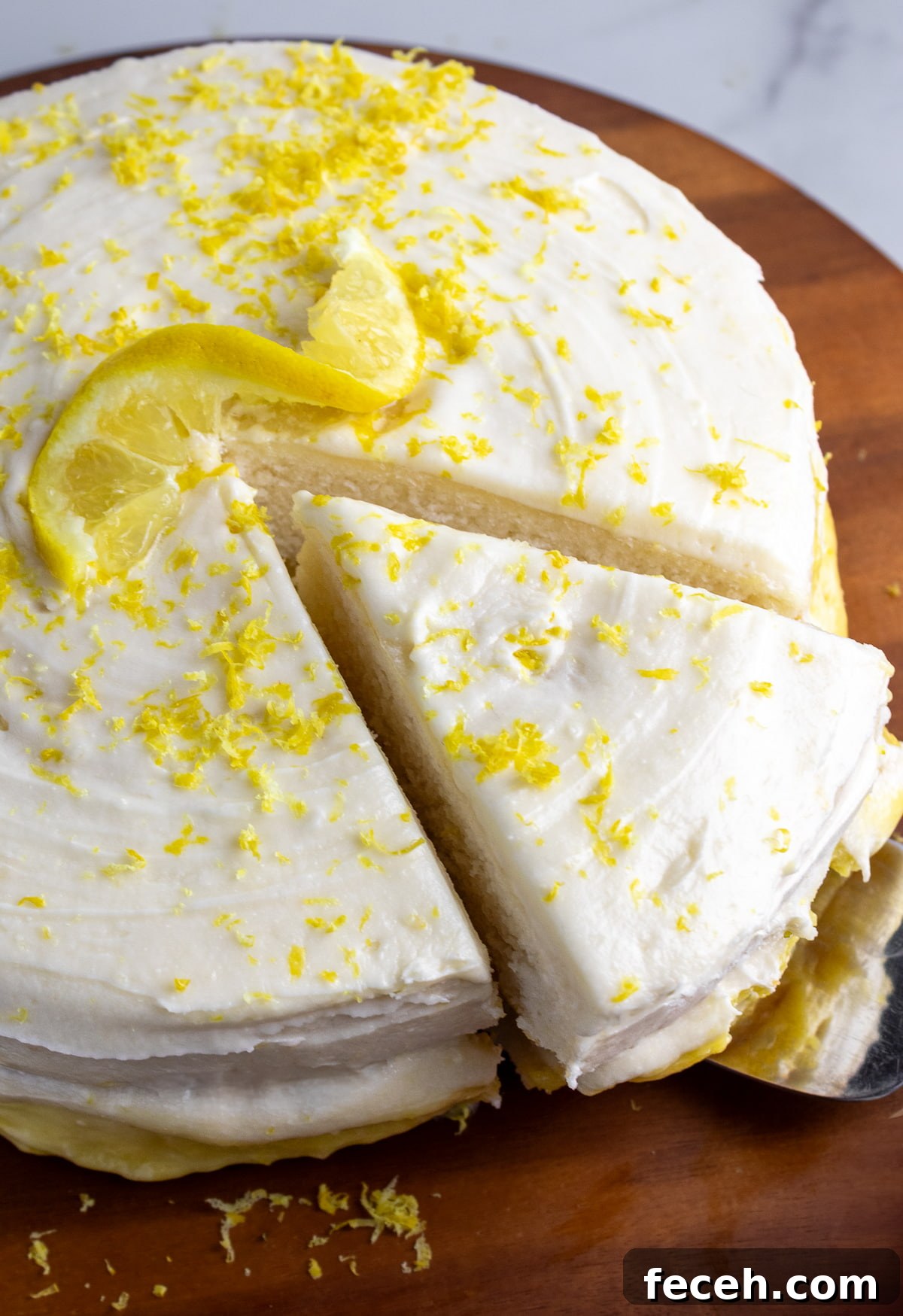 dairy-free lemon cake on wooden cake stand with on piece cut and being pulled out with a cake server utensil