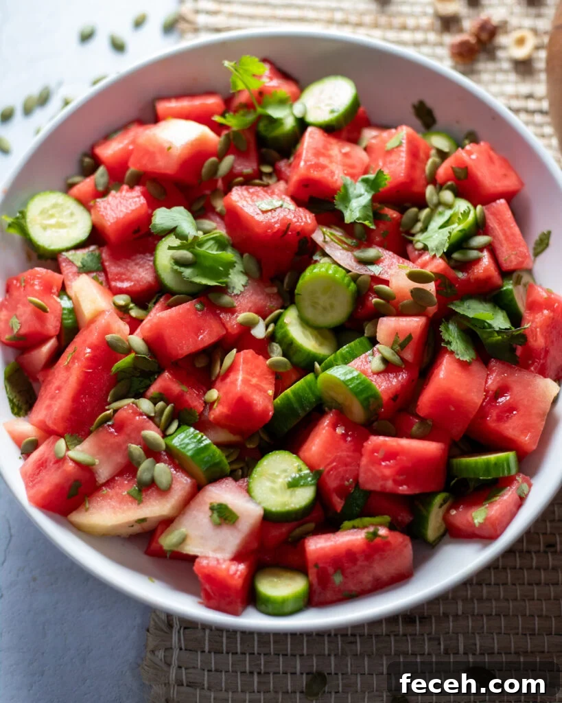 rlight blue bowl of watermelon hydration salad with watermelon chunks, cucumber chunks, pepitas and fresh cilantro in an olive oil and vinegar dressing