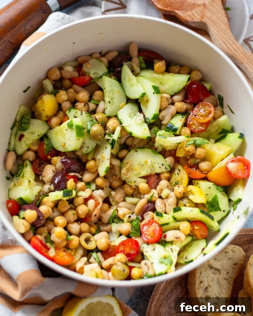 overhead view of a white serving bowl holding a dense bean salad made with two types of canned beans, cucumber, tomato, celery and olives in a simple lemon and olive oil dressing.
