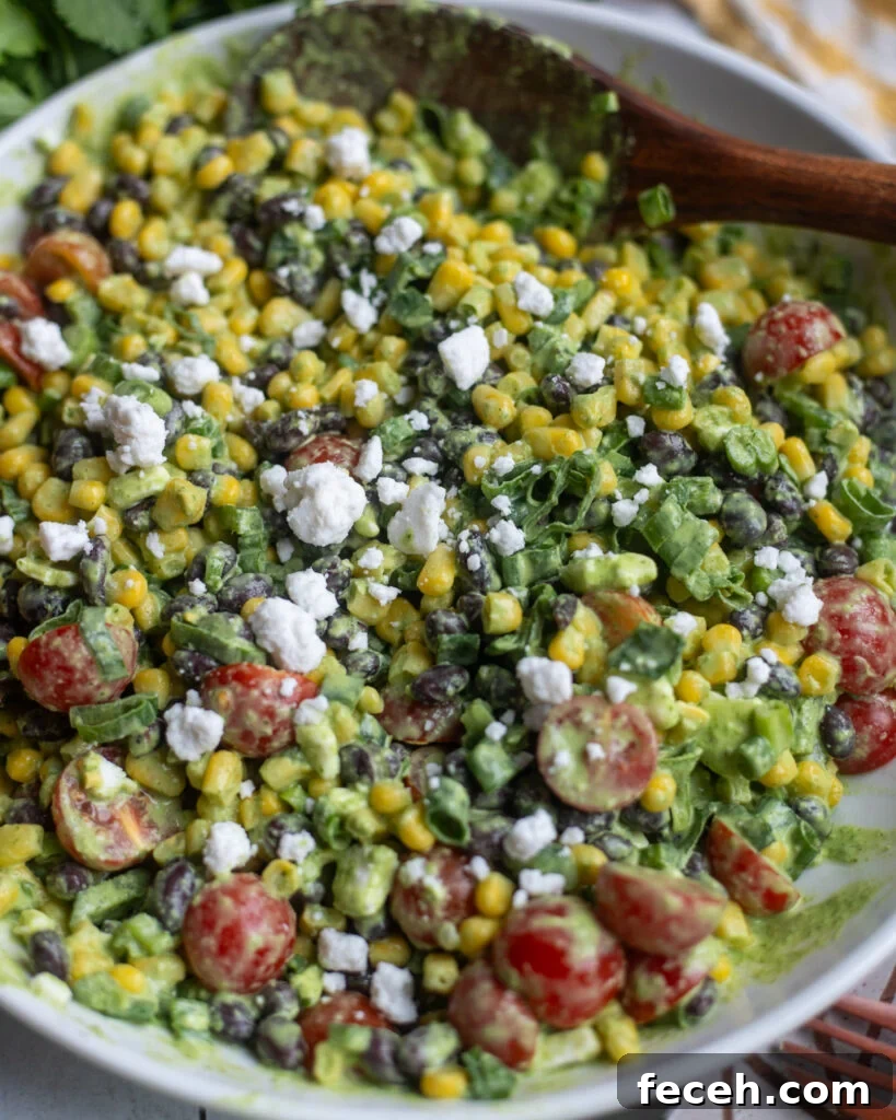 close up view of a creamy vegan black bean corn salad with cherry tomatoes, green onions, vegan feta, and a tahini cilantro dressing.