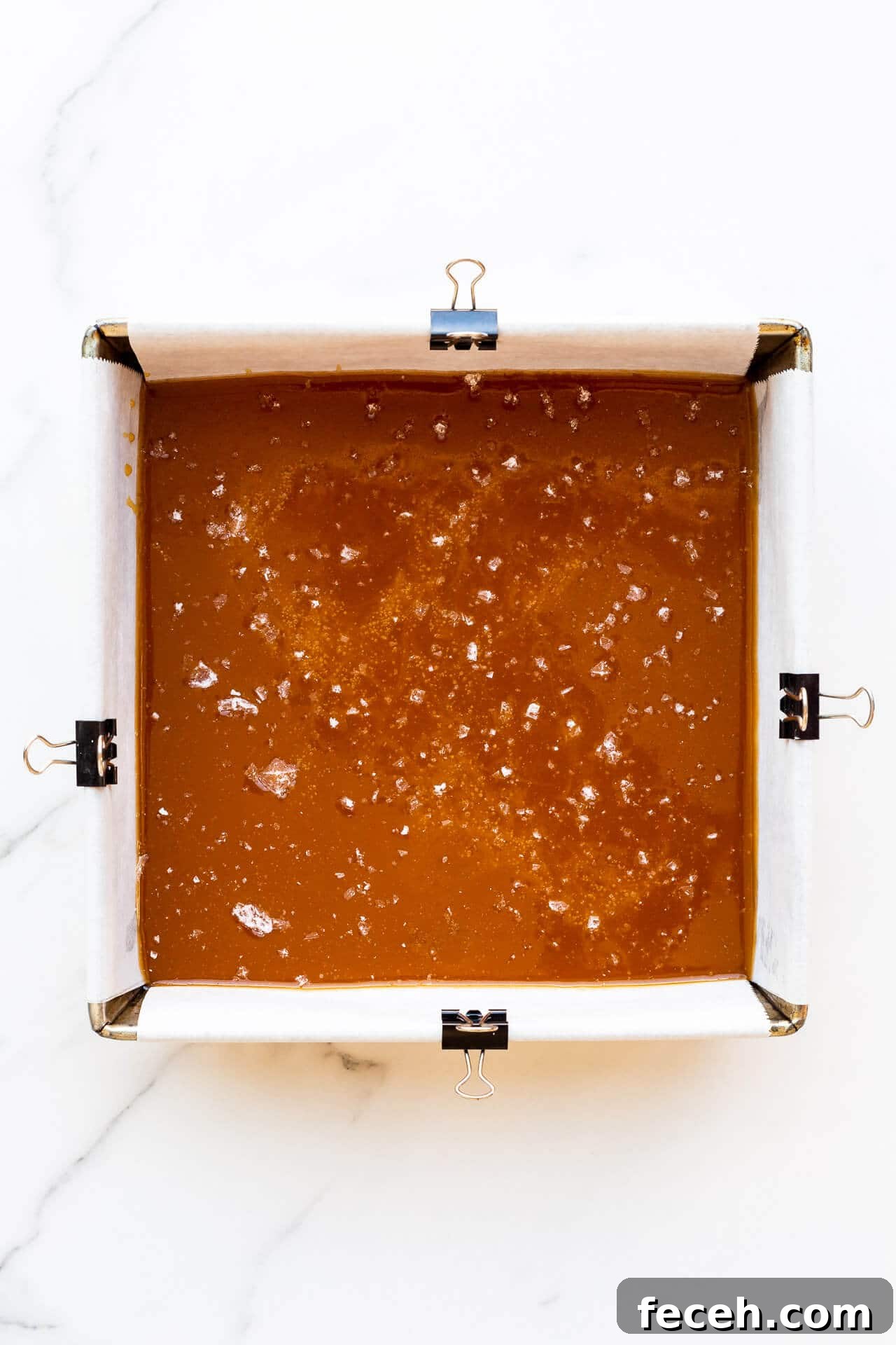 Caramels setting in an 8x8 pan lined with parchment paper clipped to sides of pan to hold it in place