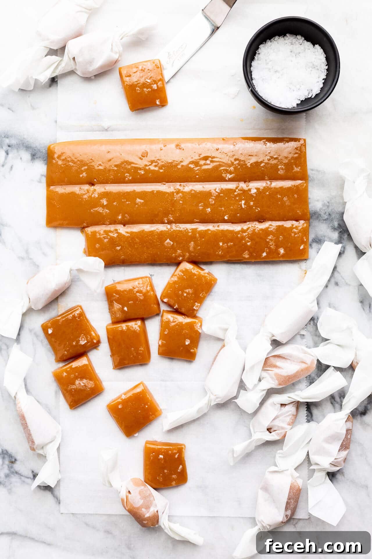 Individually wrapping homemade salted caramels in squares of parchment paper and garnishing with flaky sea salt before wrapping them