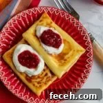 2 blintzes on red plate topped with sour cream and jam
