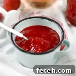 Gregory's jam in a blue cup with a small spoon and a glass of rose in the background and another jar of jam.