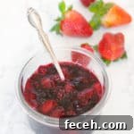 fruit compote in a glass bowl with silver spoon and fresh strawberries on the side