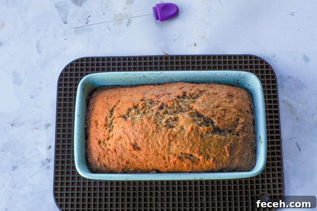 Baked Tropical Banana bread, in loaf pan, on black rectangular trivet.