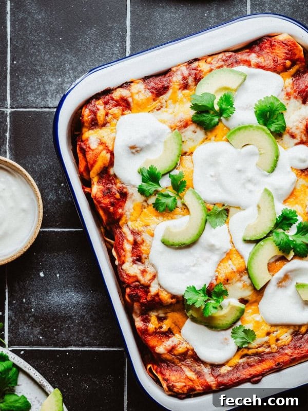 A dish of shredded beef enchiladas topped with melted cheese, avocado slices, and cilantro.
