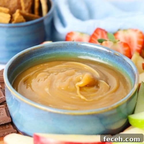 Homemade caramel dip in a bowl next to sweet crackers, fruit and chocolate for dipping.