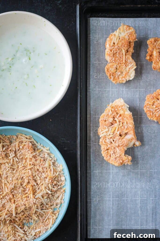 Breading cauliflower on a baking sheet next to a bowl with coconut milk and a bowl with breading.