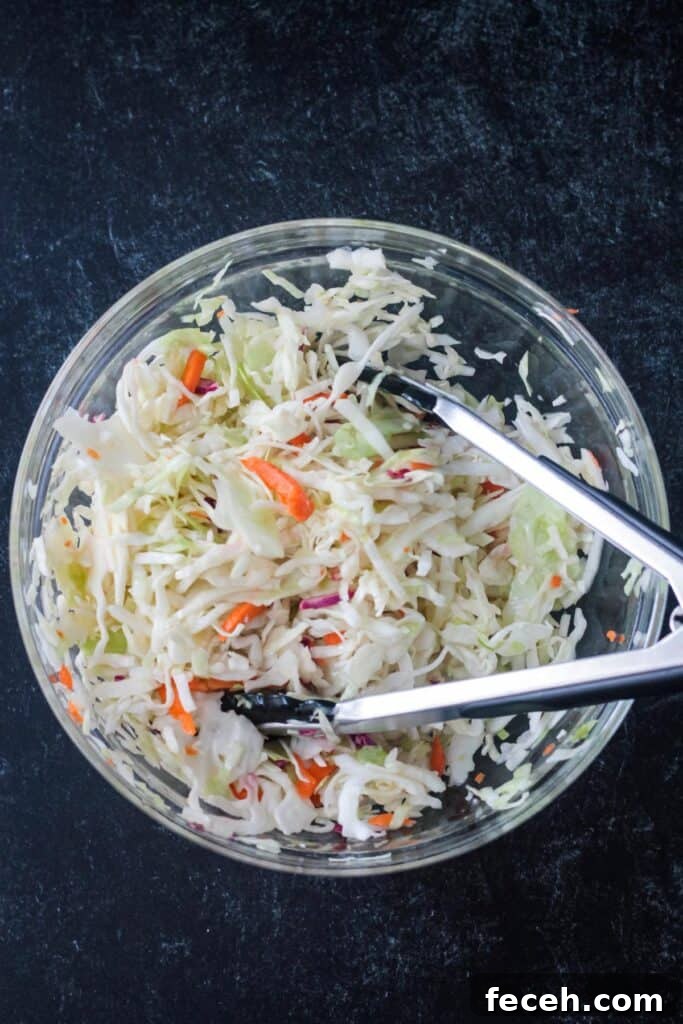 Coleslaw in a glass bowl with serving tongs.