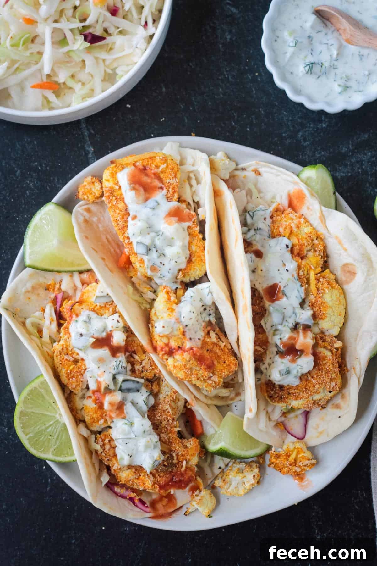 Overhead view of three folded cauliflower tacos on a plate with sauce.