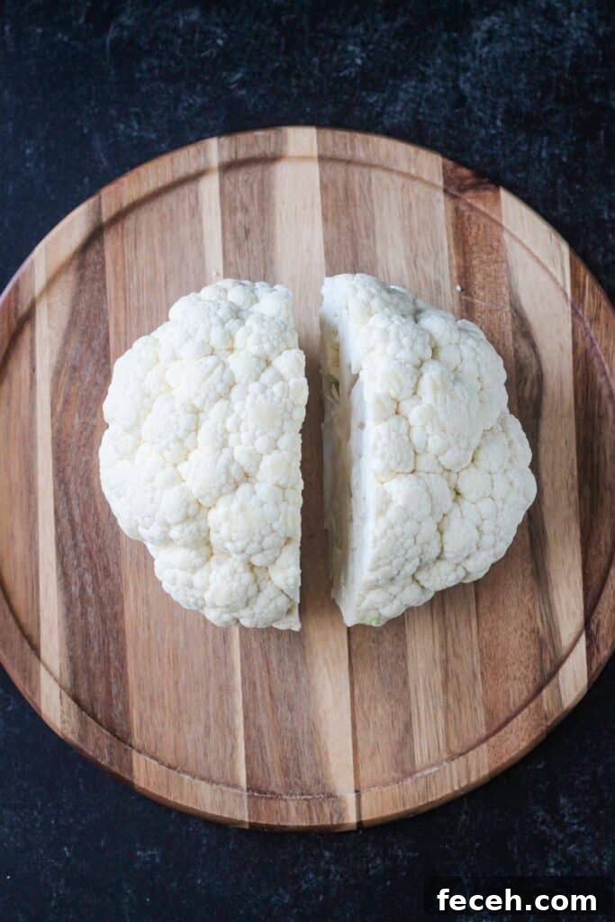 A large cauliflower cut into half on a cutting board.