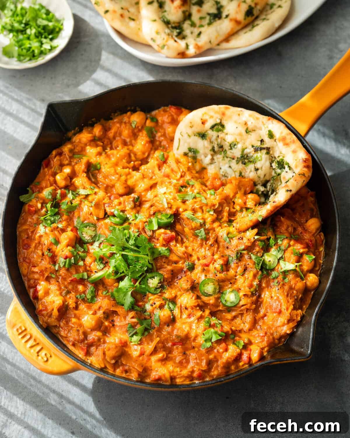Curry topped with cilantro and serrano slices, served in a skillet with naan.