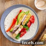 A plate with crispy buffalo tofu wrap topped with avocado, red peppers, lettuce, red onions and a homemade buffalo ranch sauce.
