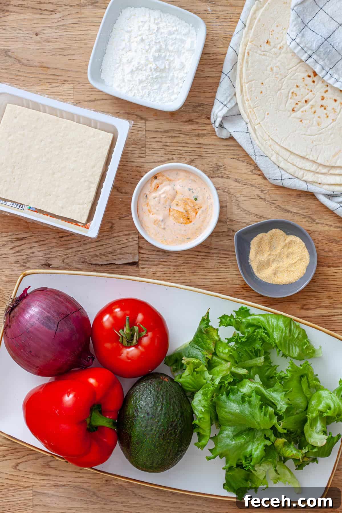 Ingredients for crispy buffalo tofu wraps on a butcherblock cutting board.