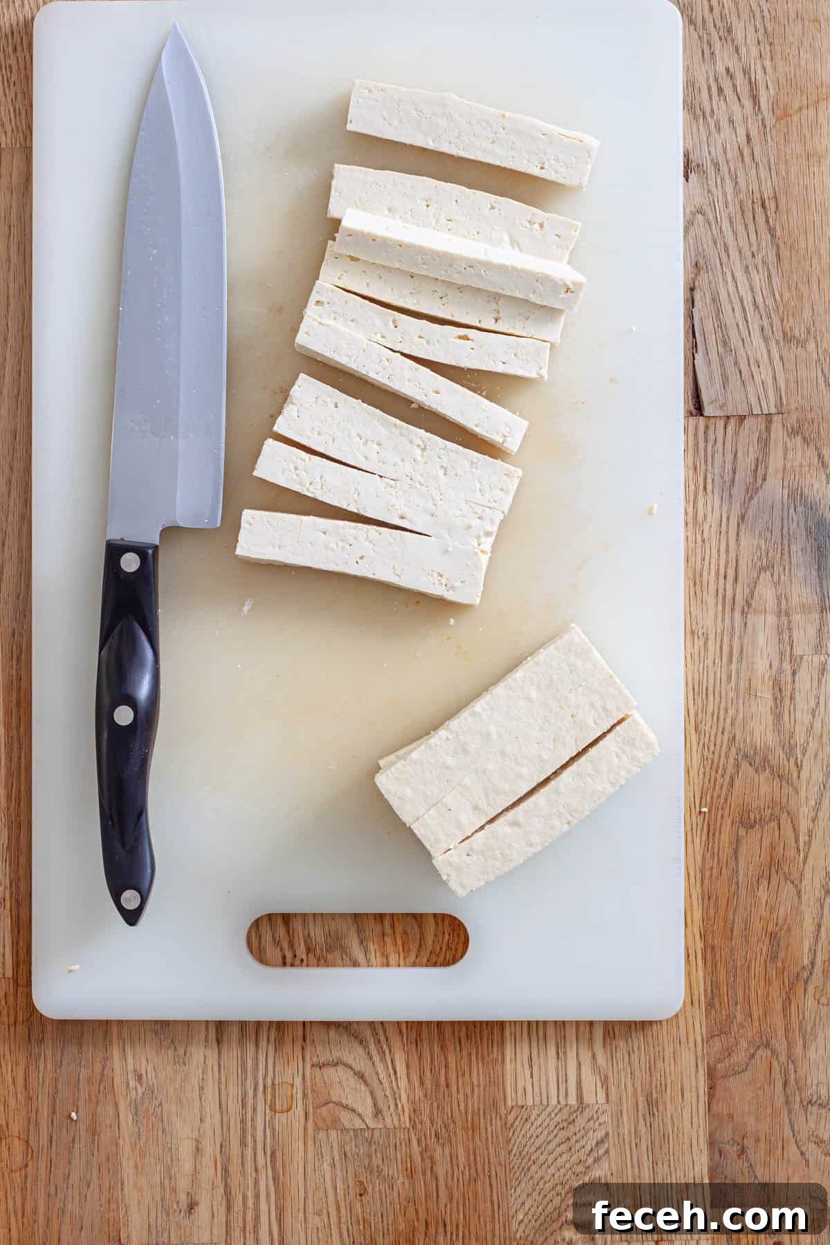 Tofu on a cutting board getting cut into strips for tofu wraps.