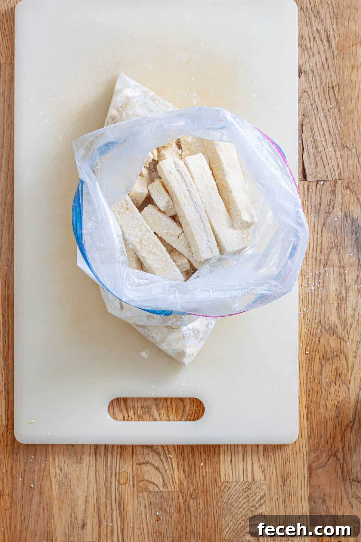 Strips of tofu in a zip-top bag with cornstarch and seasoning getting ready to be baked.
