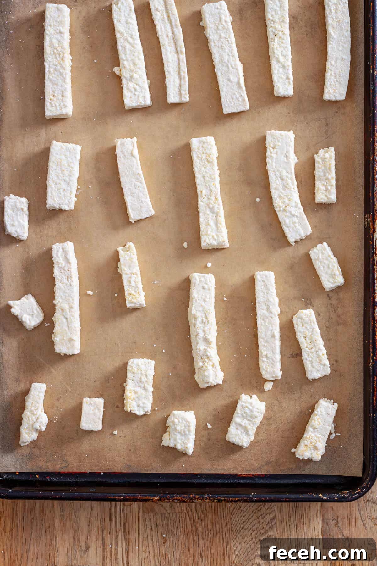 Strips of tofu coated in cornstarch on a parchment-lined baking sheet.