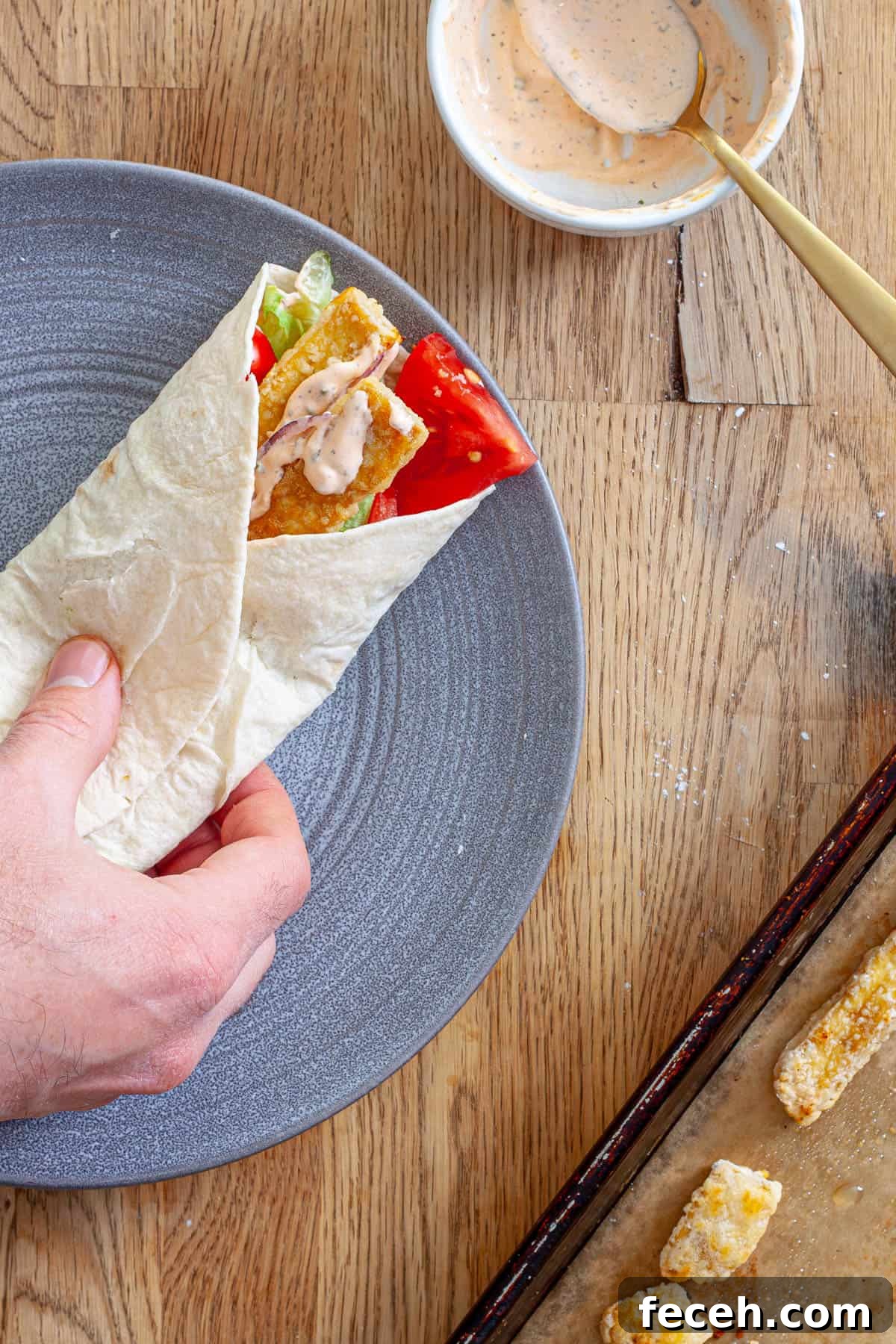 A crispy tofu wrap on a plate getting assembled.